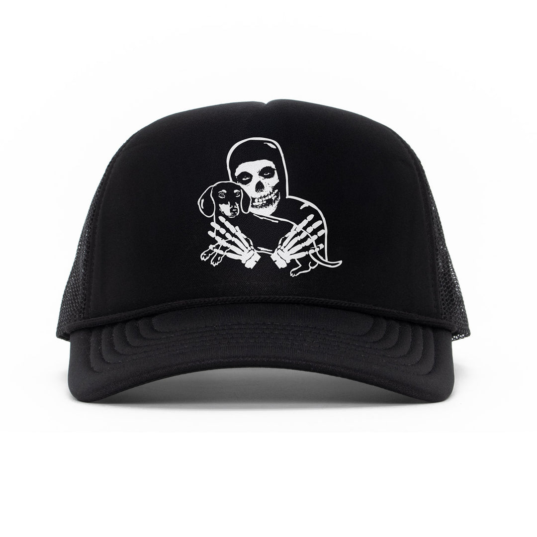 Black trucker hat featuring a white graphic of a crimson skeleton figure holding a small dachshund, shown against a plain white background.