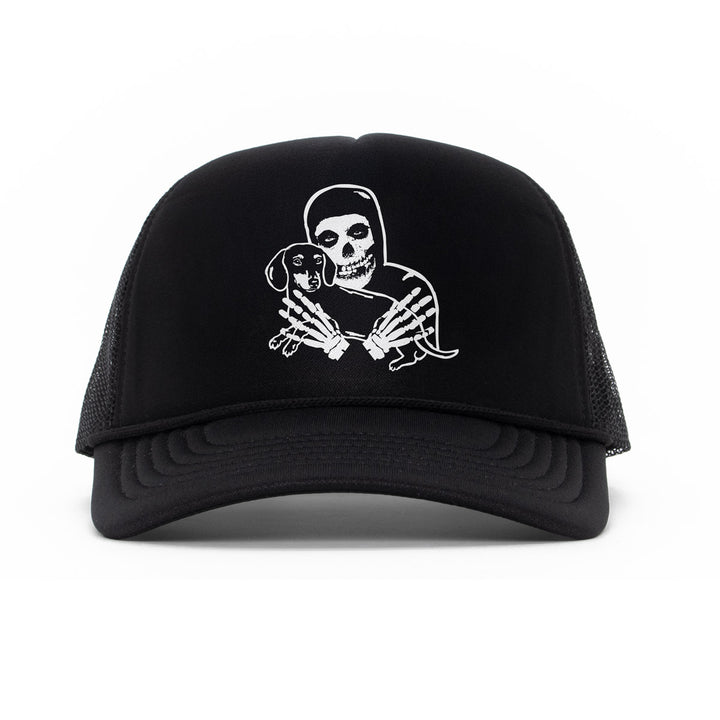 Black trucker hat featuring a white graphic of a crimson skeleton figure holding a small dachshund, shown against a plain white background.