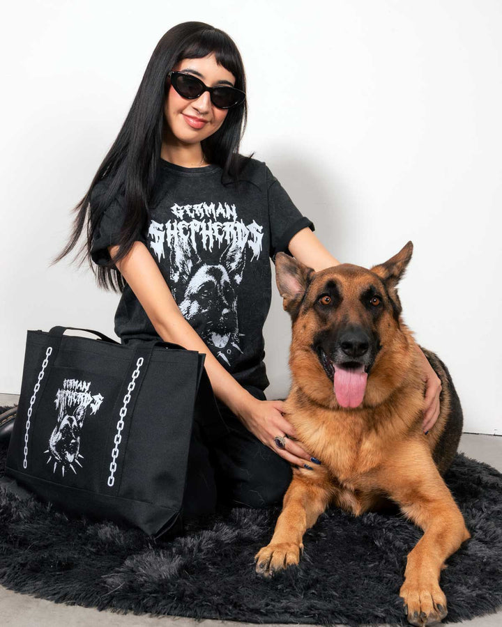 A woman wearing a black graphic t-shirt and sunglasses sits on a black shag rug next to a German Shepherd dog, holding a large black tote bag with a white dog graphic and the text 'German Shepherds'.