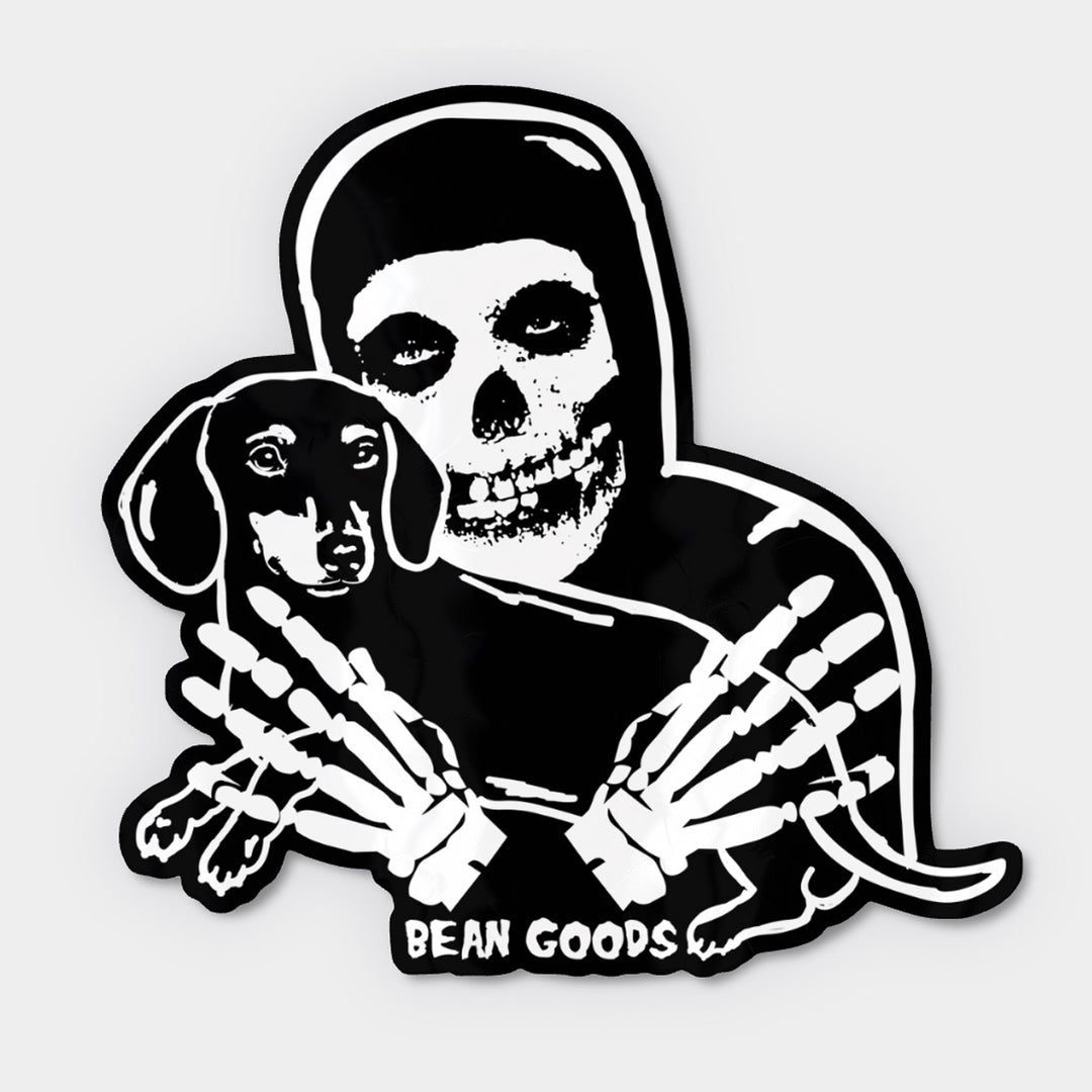A die-cut sticker featuring a black and white graphic of a crimson skeleton holding a dachshund, with the text 'BEAN GOODS' at the bottom, shown on a light gray background.
