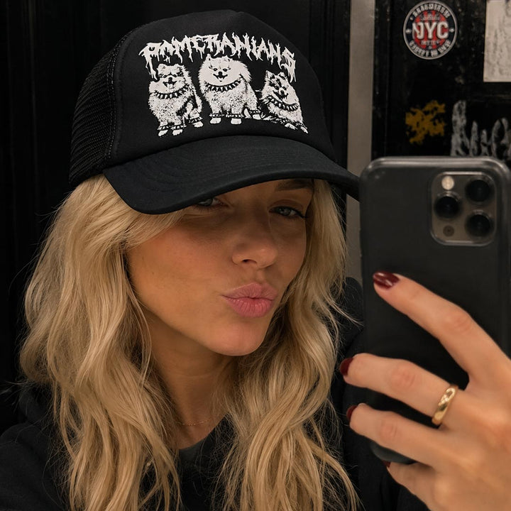 Person wearing a black cap with graphic design, holding a phone.
